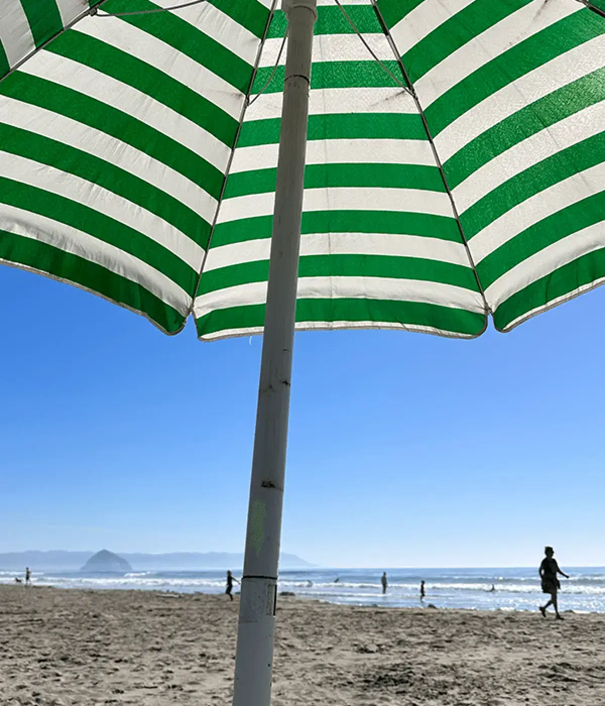 Green-and-white striped beach umbrella on a sandy shore under a clear sky